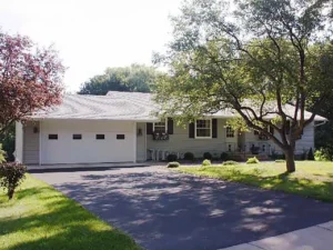Bland house front with garage offset to front and blue gray metal siding with black shutters.