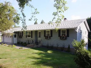 Bland house front with blue gray metal siding and black shutters.