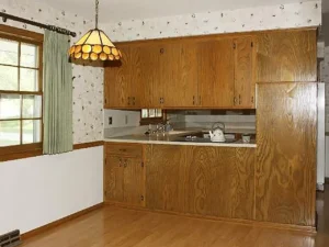 Dark full height cabinetry wall separating kitchen and dinette with dated wallpaper and fixtures.